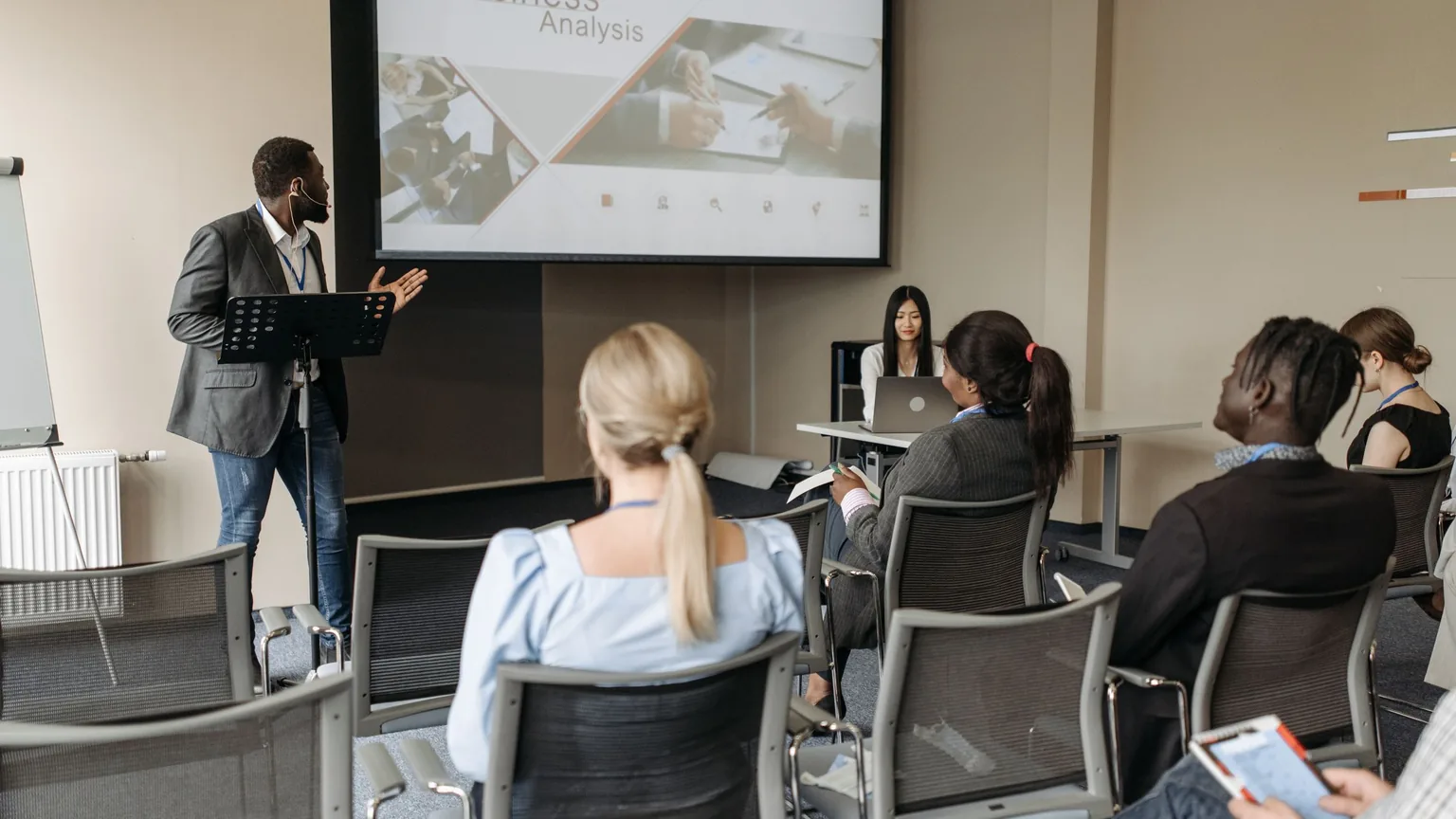A speaker presenting to a seated group of professionals at an early meeting