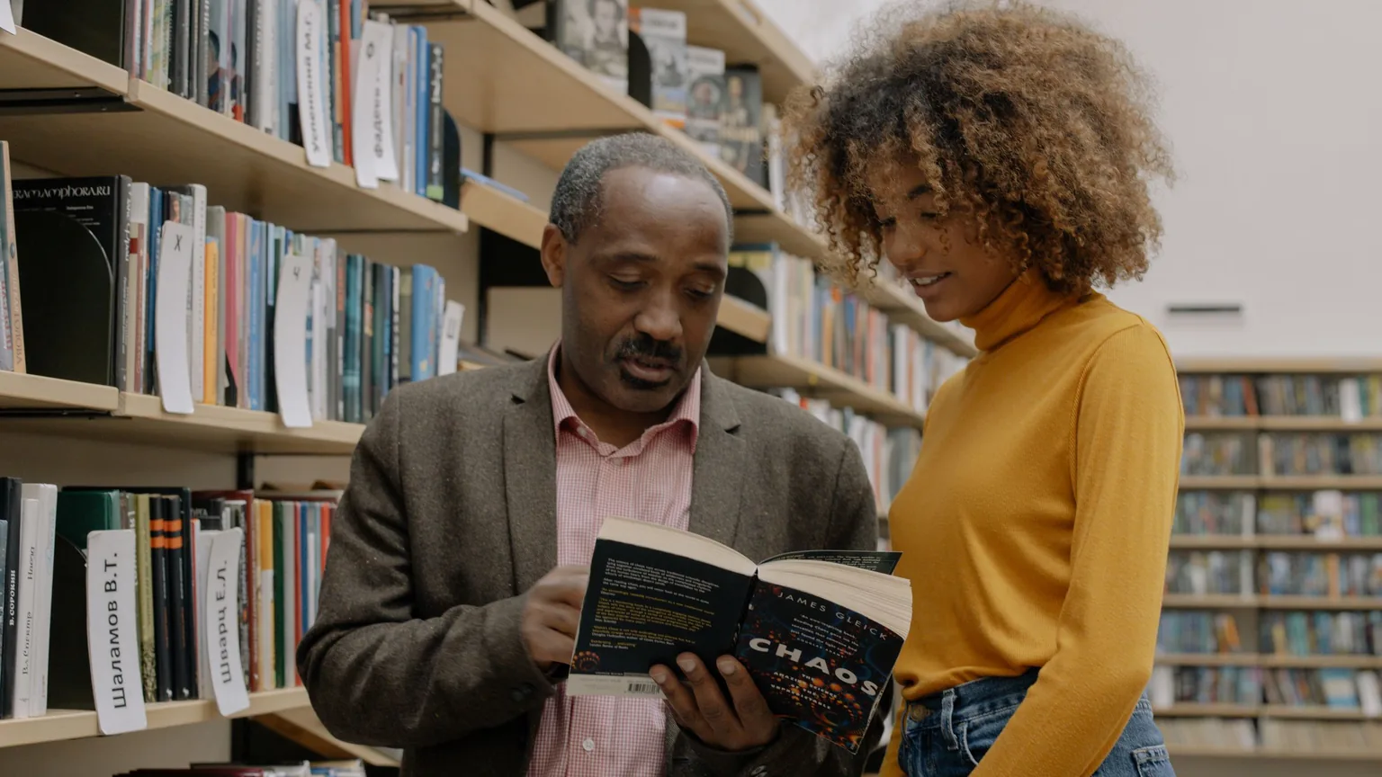 An experienced volunteer showing a newer member how the library's records work, between the shelves