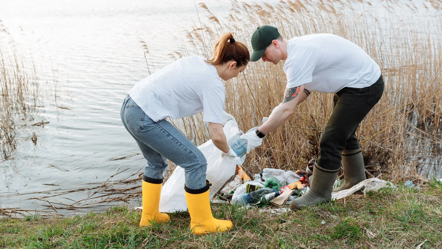 Two volunteers picking up rubbish along a riverbank during a clean-up