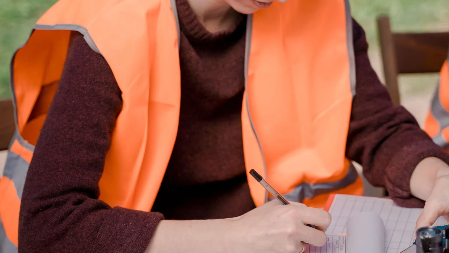 A volunteer in a hi-vis vest filling in a long paper form at a folding table outdoors
