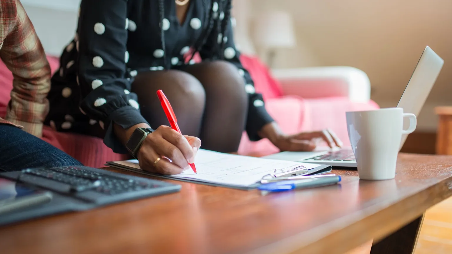 A woman at a table copying details from a paper form into a laptop