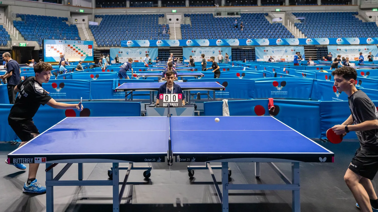Players competing at a table tennis tournament in a large indoor hall