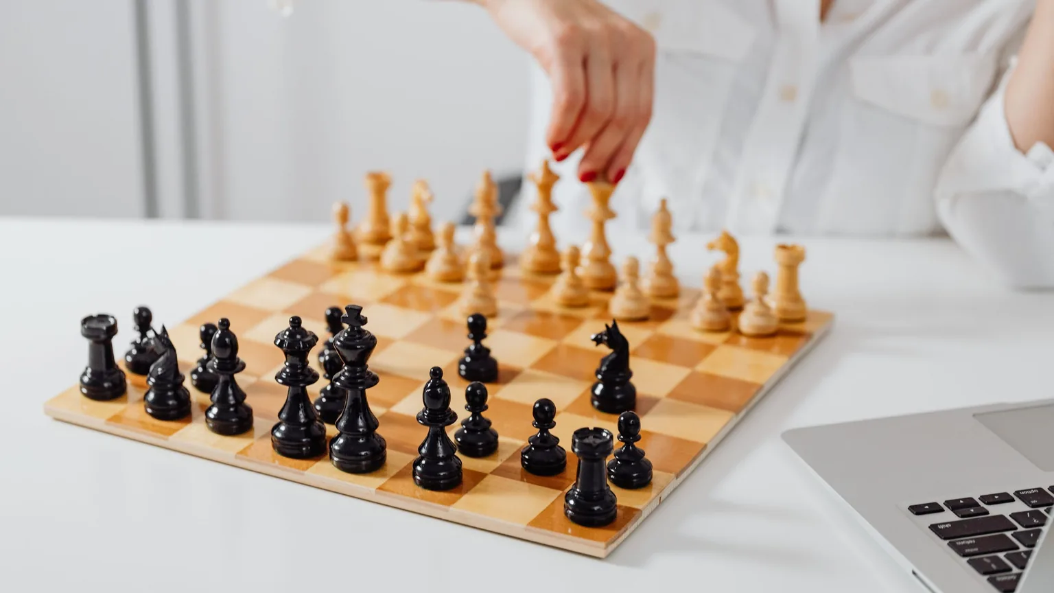 A hand moving a chess piece next to an open laptop