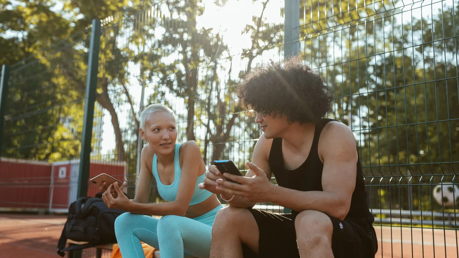 Two players on a bench at the edge of the court checking their phones between games
