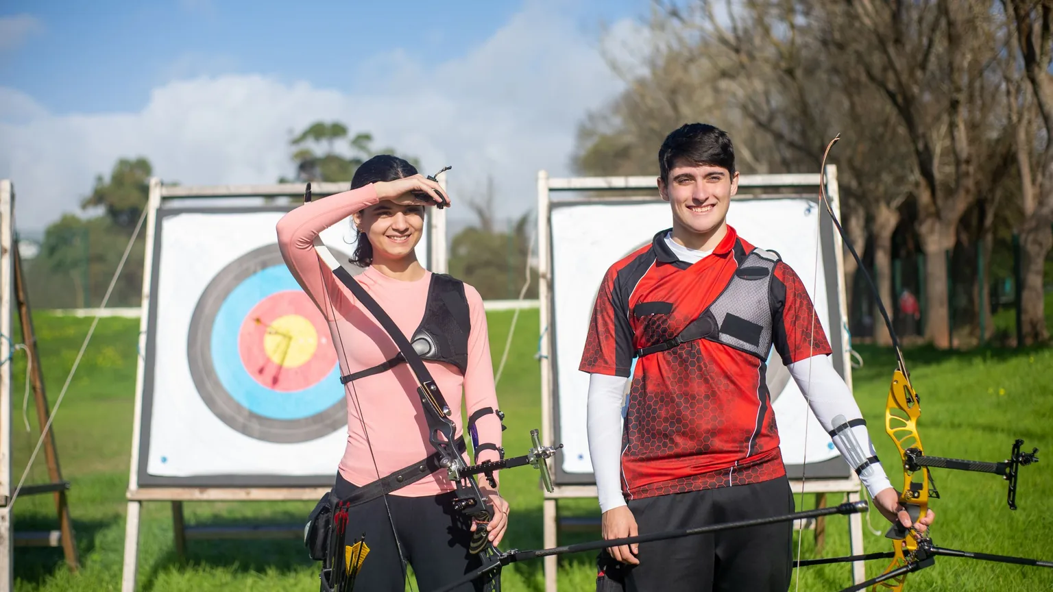 Two archery club members with their bows beside targets at an outdoor range