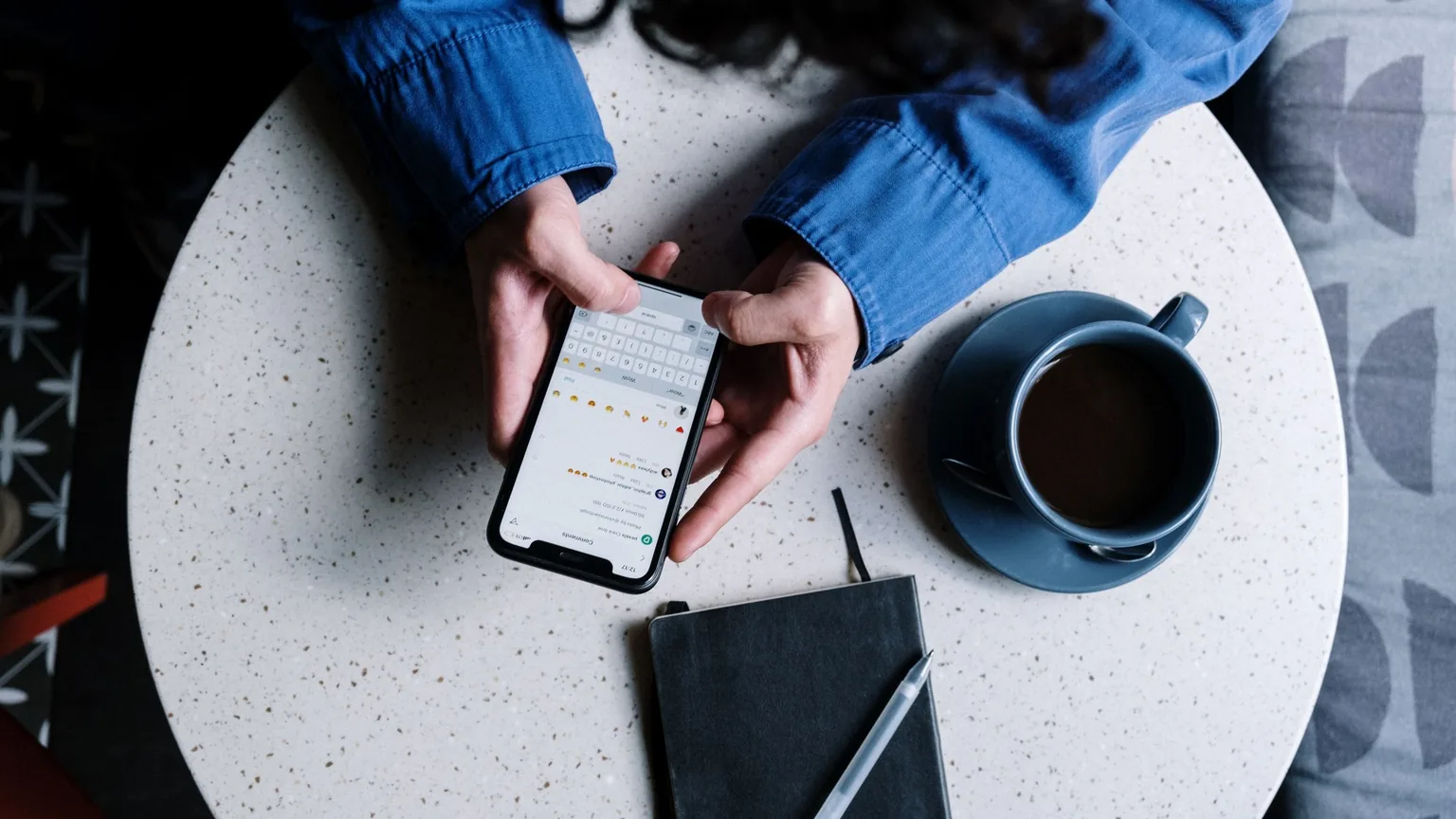 A phone, a coffee and a notebook on a cafe table, seen from above