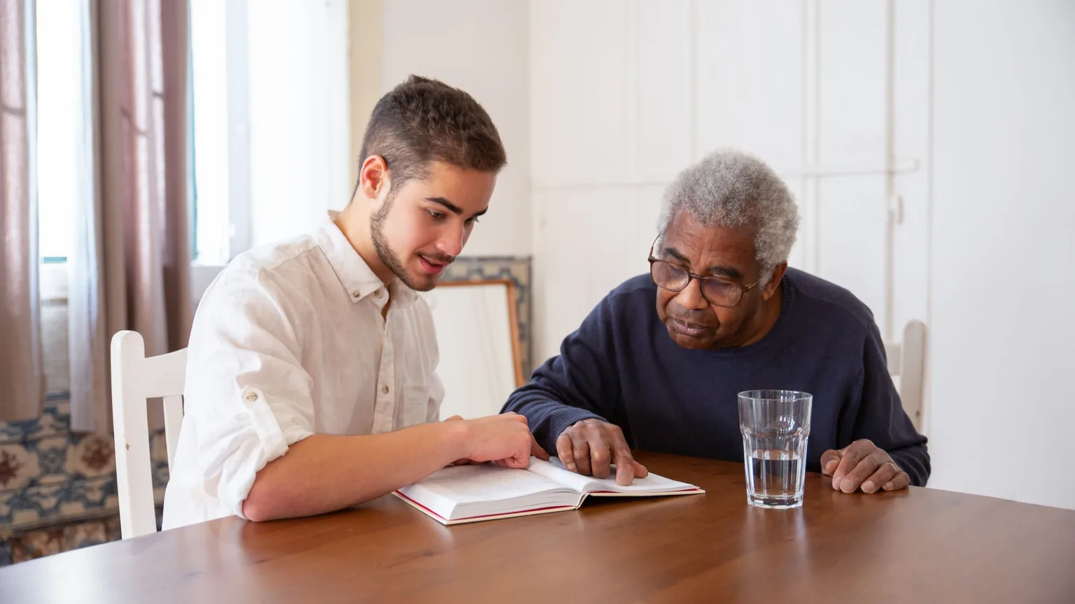 A young man and an older man sitting together at a table over a book