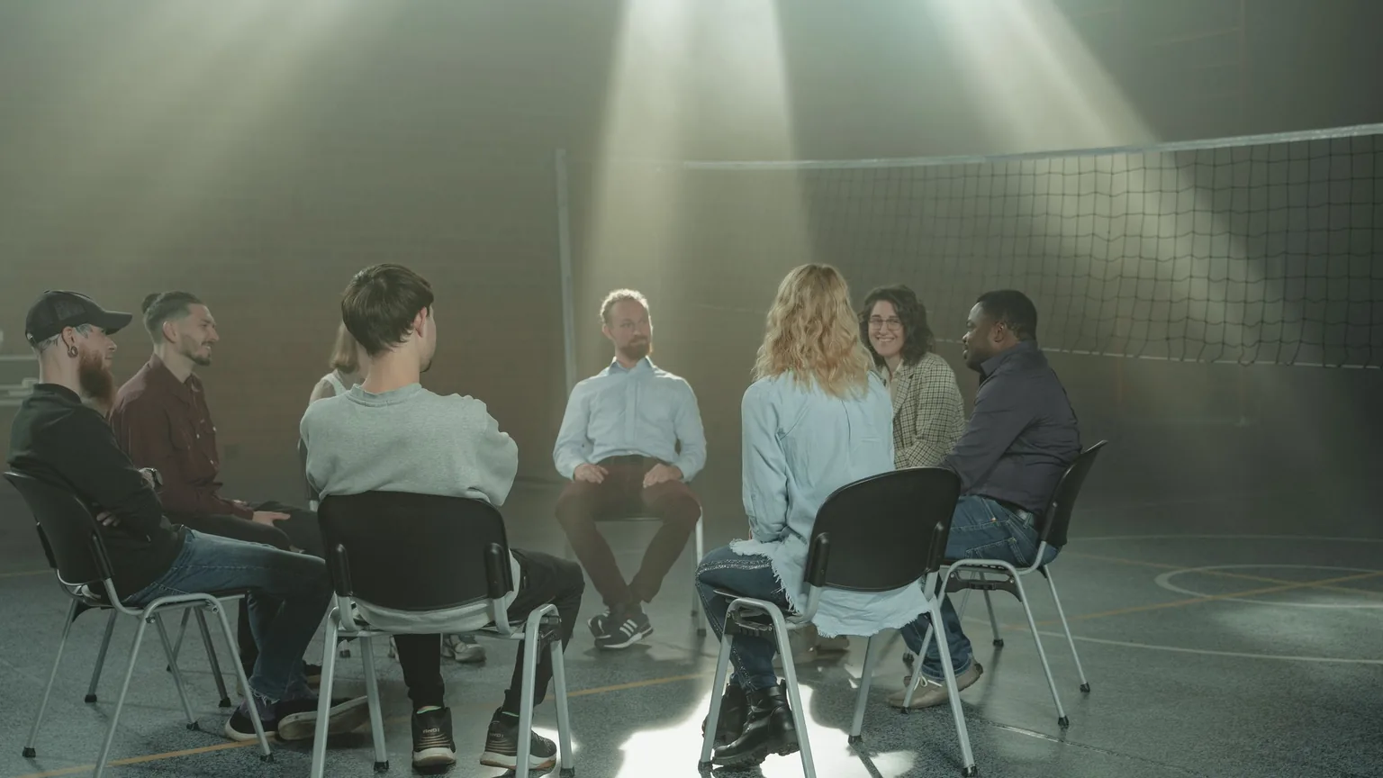 A small group sitting in a circle of chairs at their first meeting in a sunlit hall