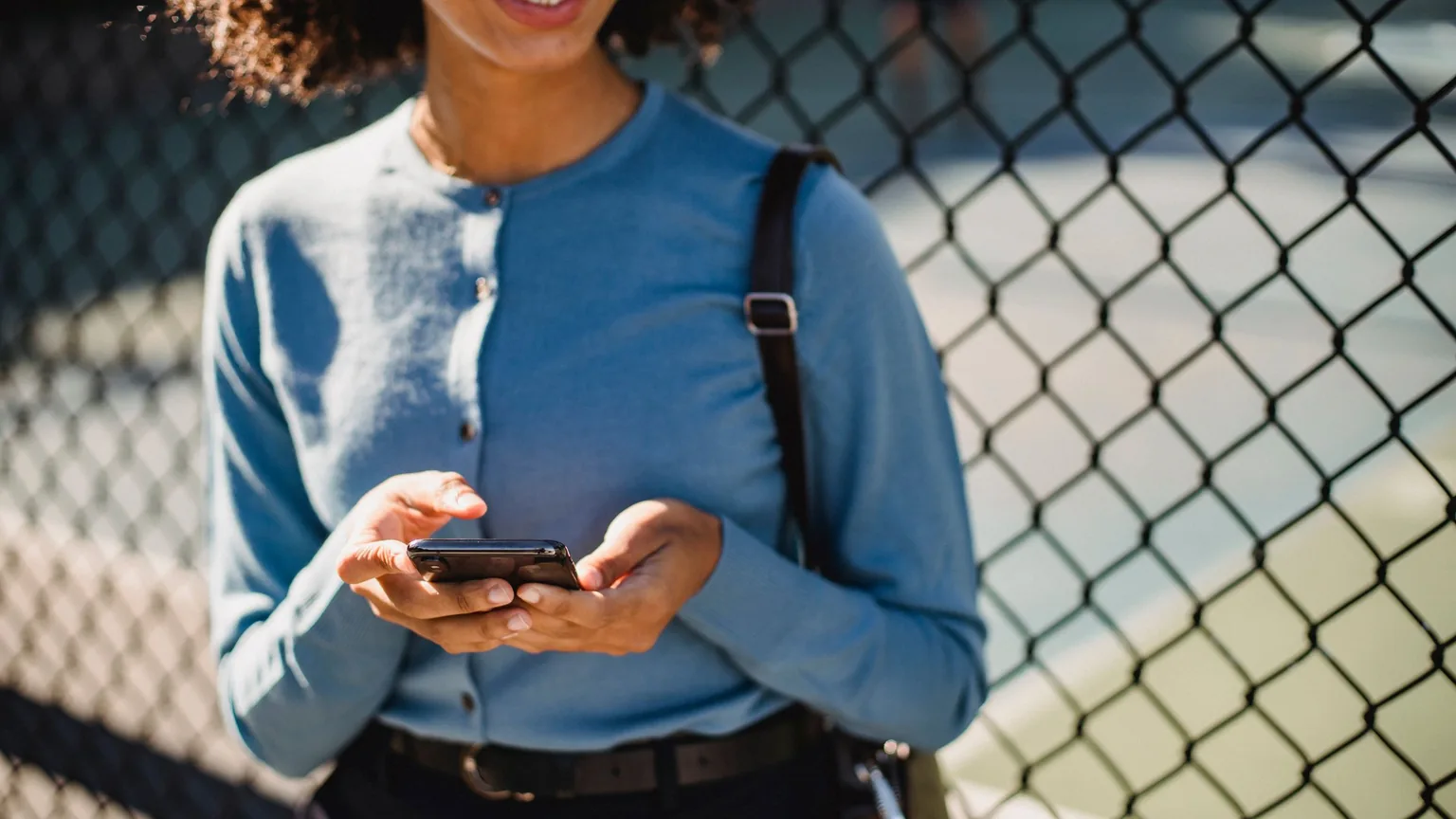 A woman completing a sign-up on her phone by the court fence