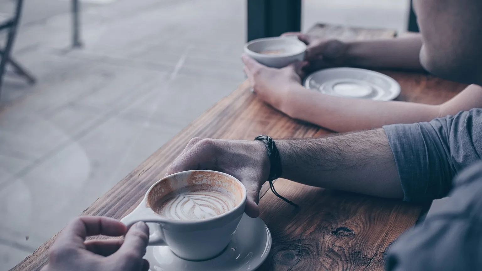 Two friends with coffees across a cafe table