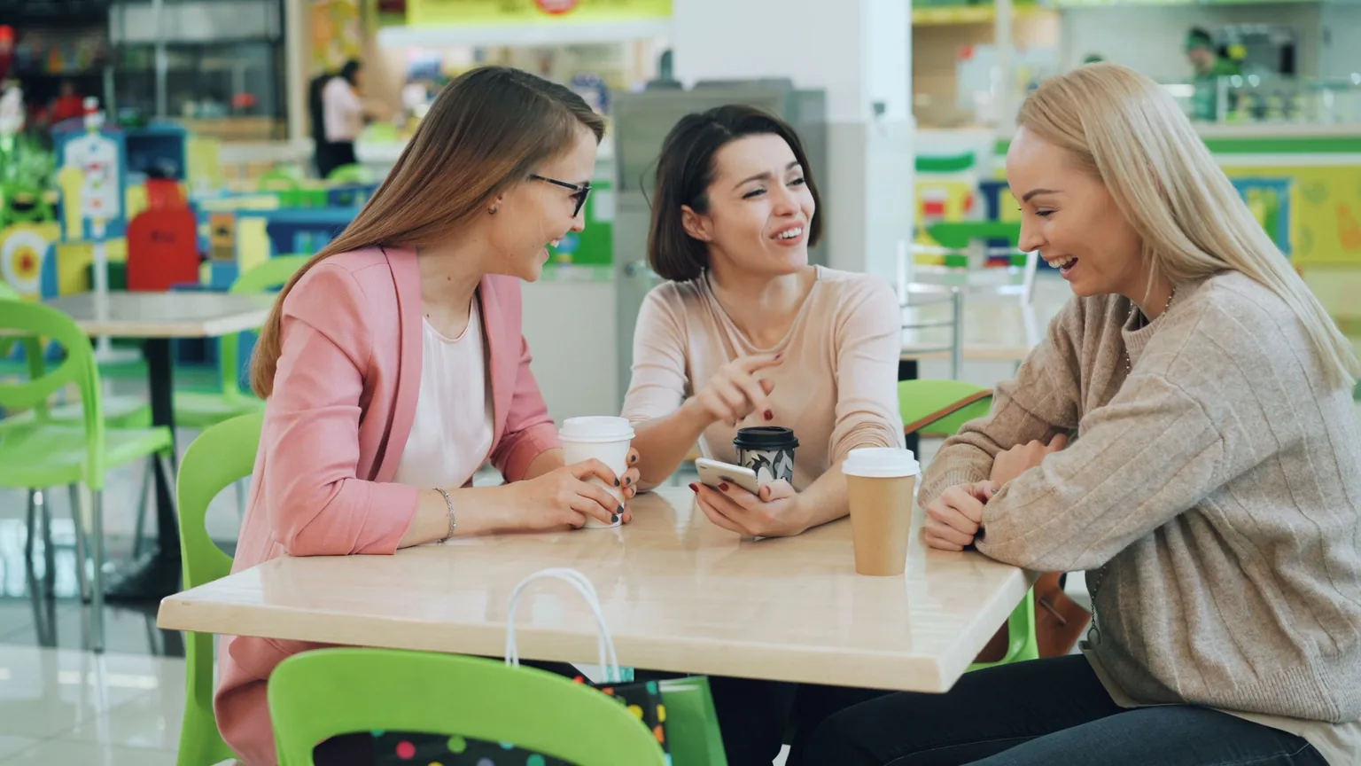 Three friends laughing together over coffee at a cafe table