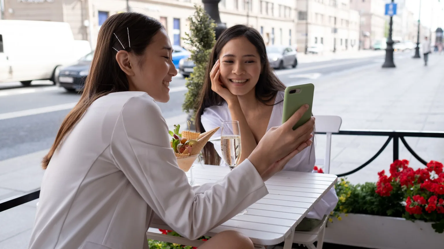 A woman showing her friend something on her phone at a cafe table