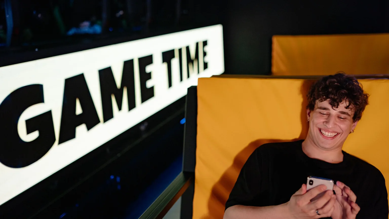 A young gamer smiling at his phone in a gaming lounge