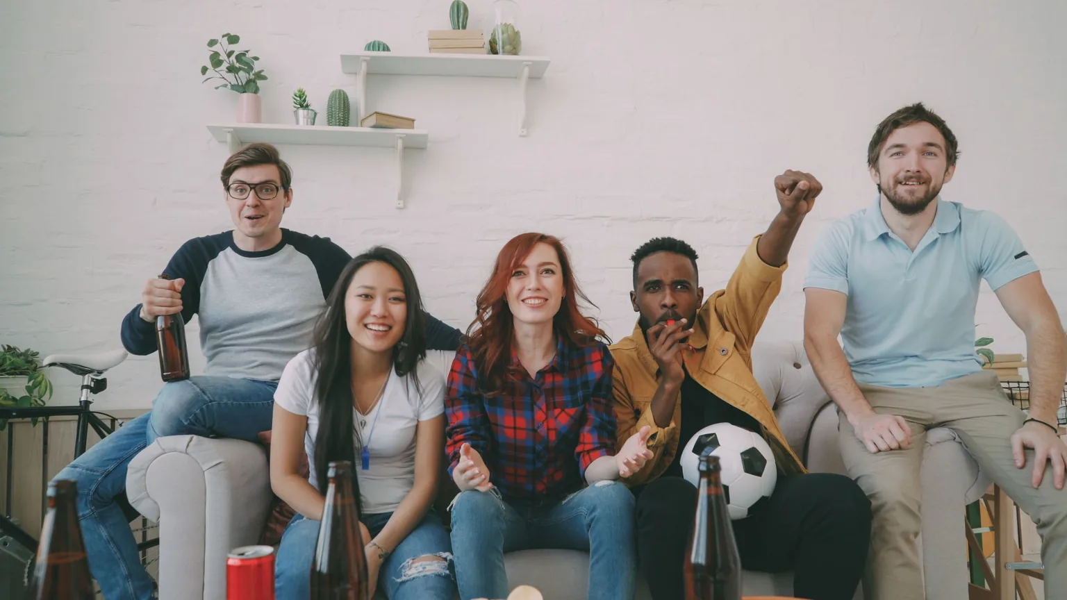 Friends cheering together on a sofa while watching a football match