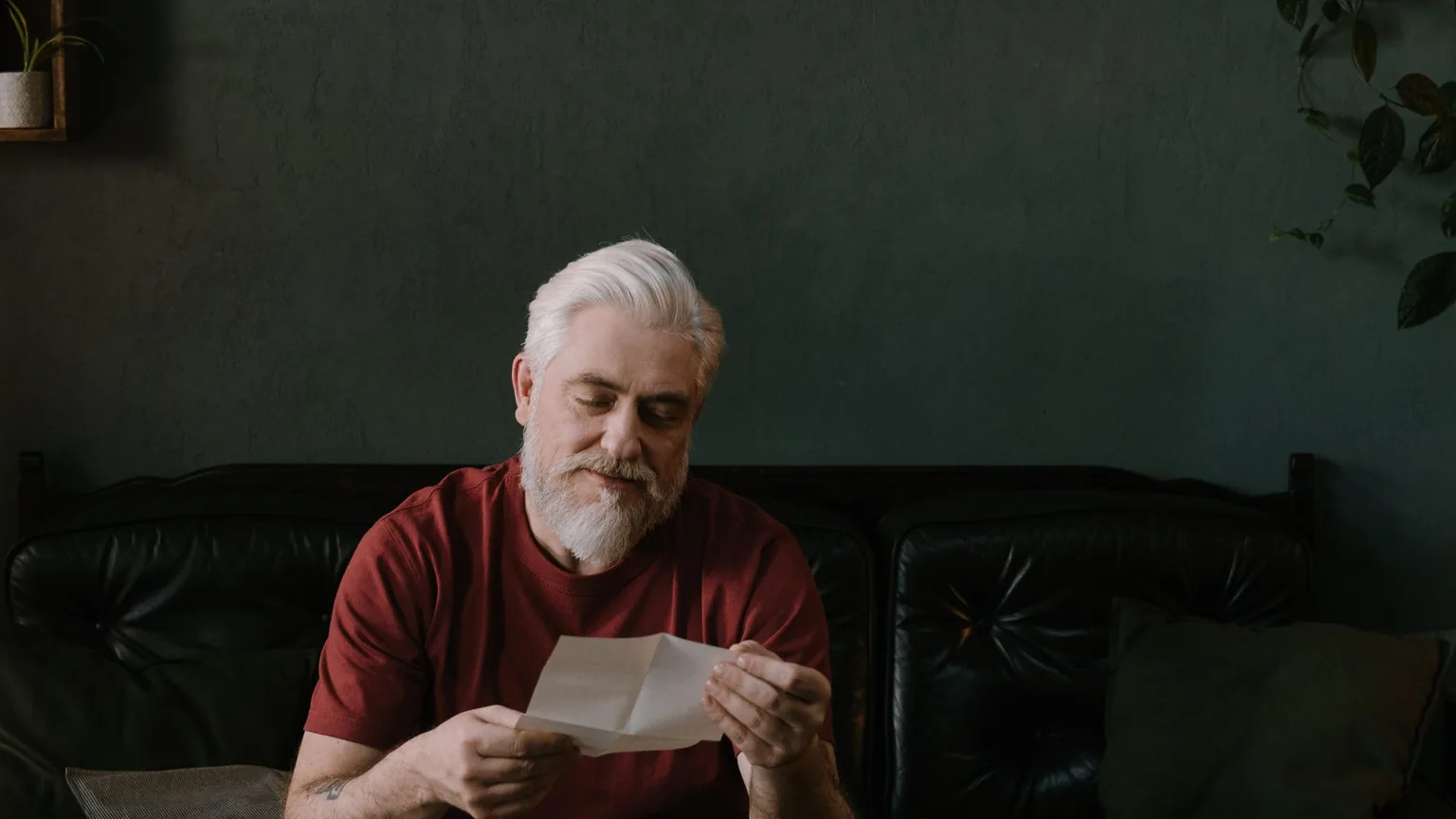 An older man at home reading a letter at the kitchen table