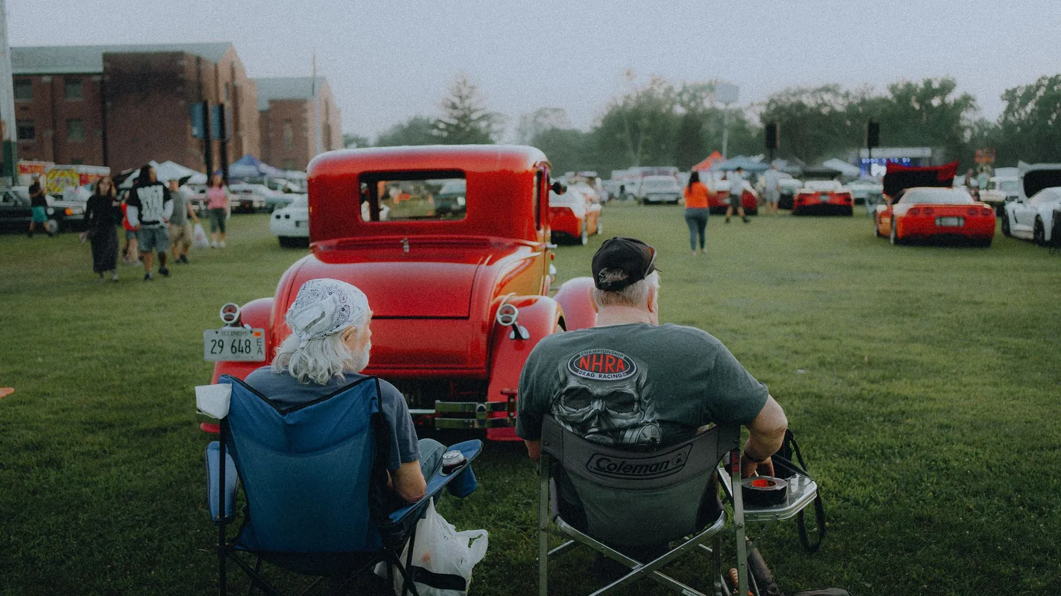 Classic car owners relaxing in folding chairs beside a vintage car at a show