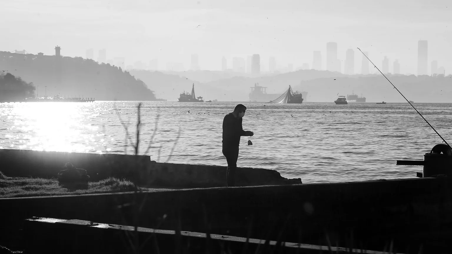 An angler on the harbour wall at first light, city skyline behind