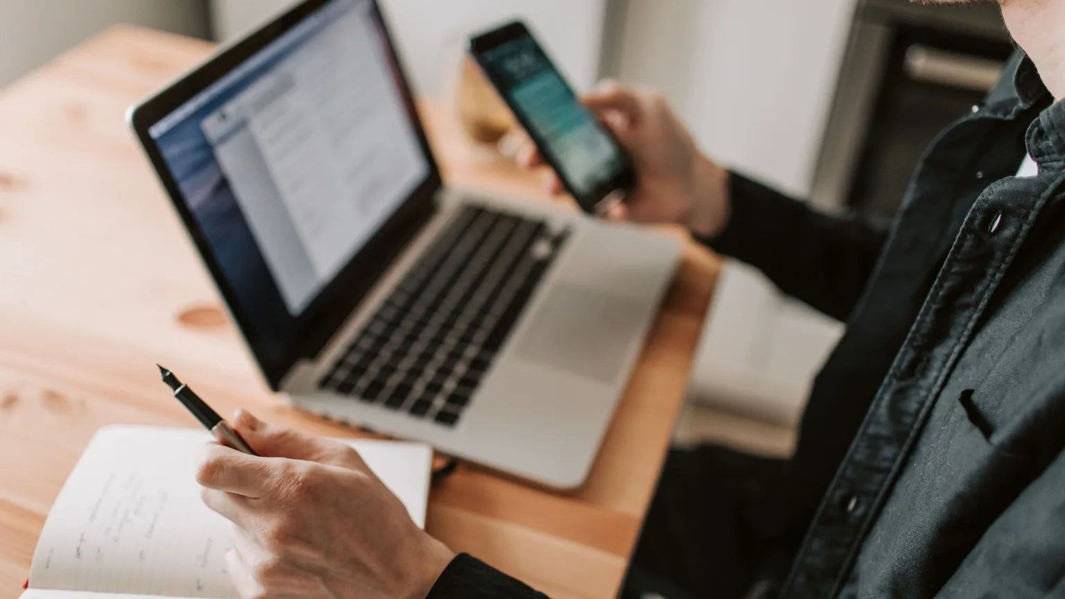 A club organiser at home with a phone in hand and a laptop and notebook open on the desk