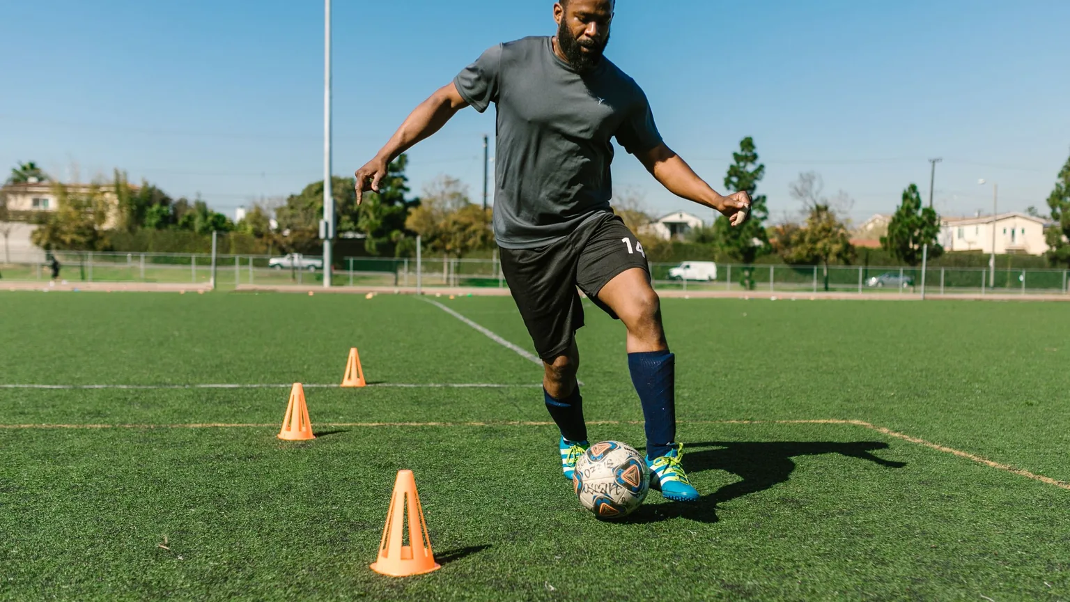 A footballer running a drill through cones on a local pitch