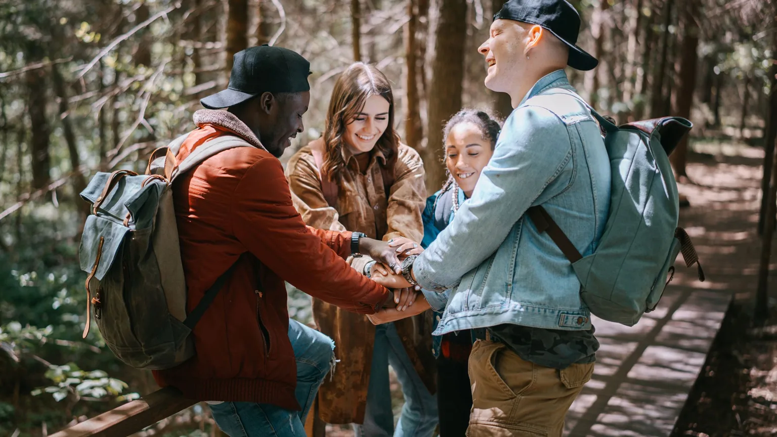 Four hikers putting their hands together on a forest bridge before a trek