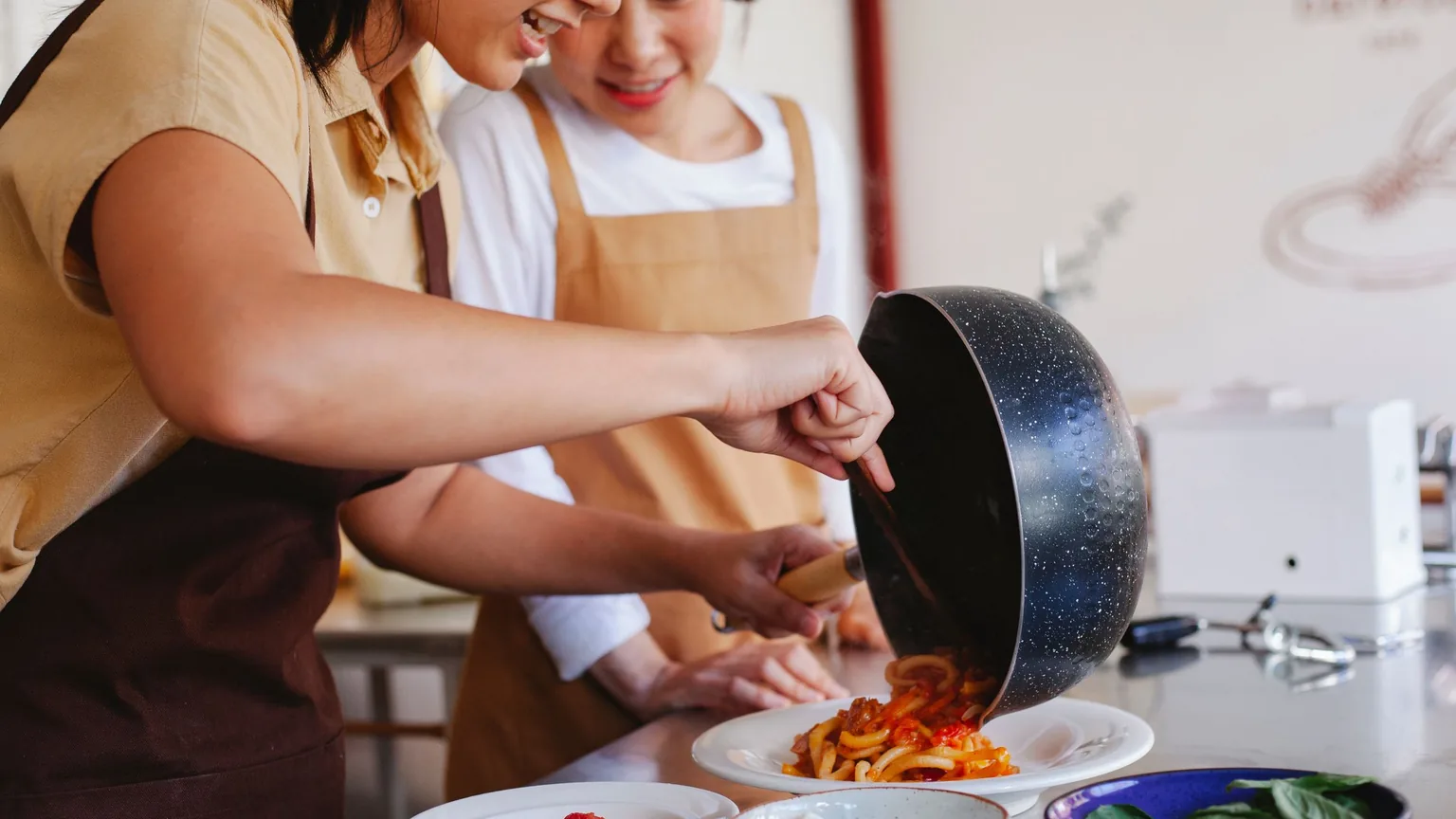 Two members in aprons plating up food together in a kitchen