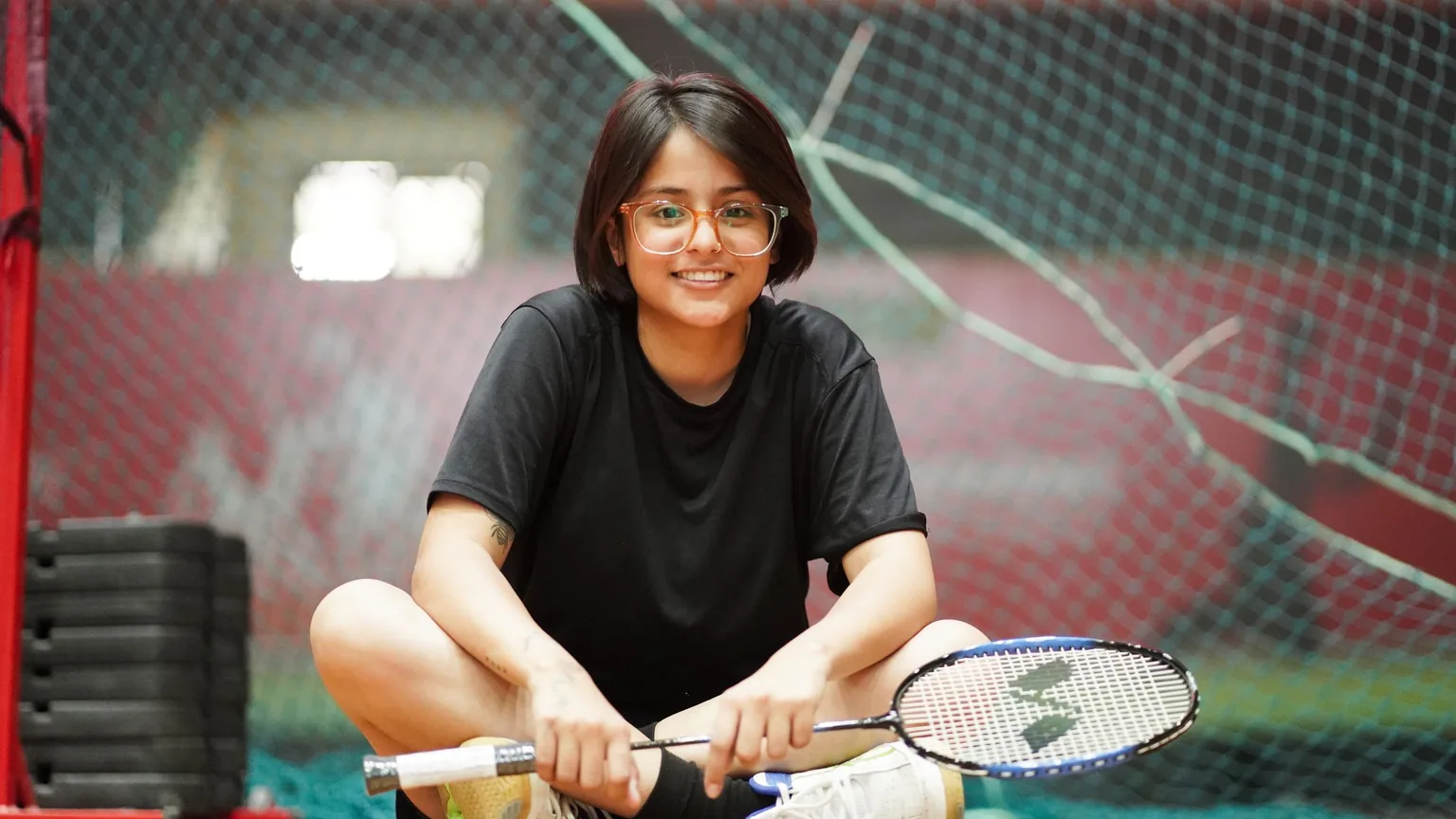 A player sitting at the side of the badminton court with her racket, taking a breather