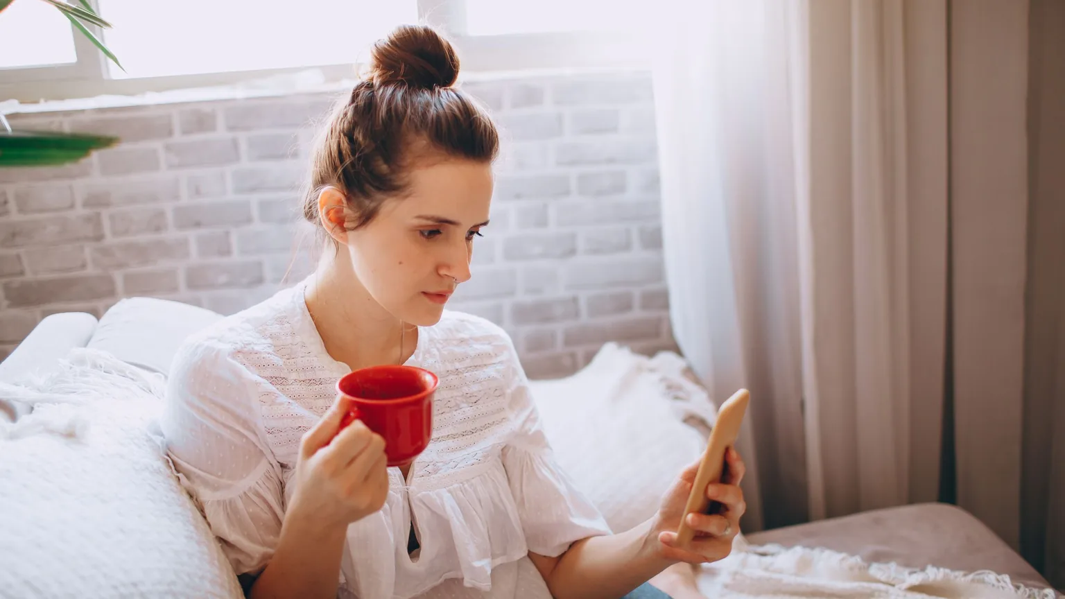A member reading on her phone over a morning coffee at home