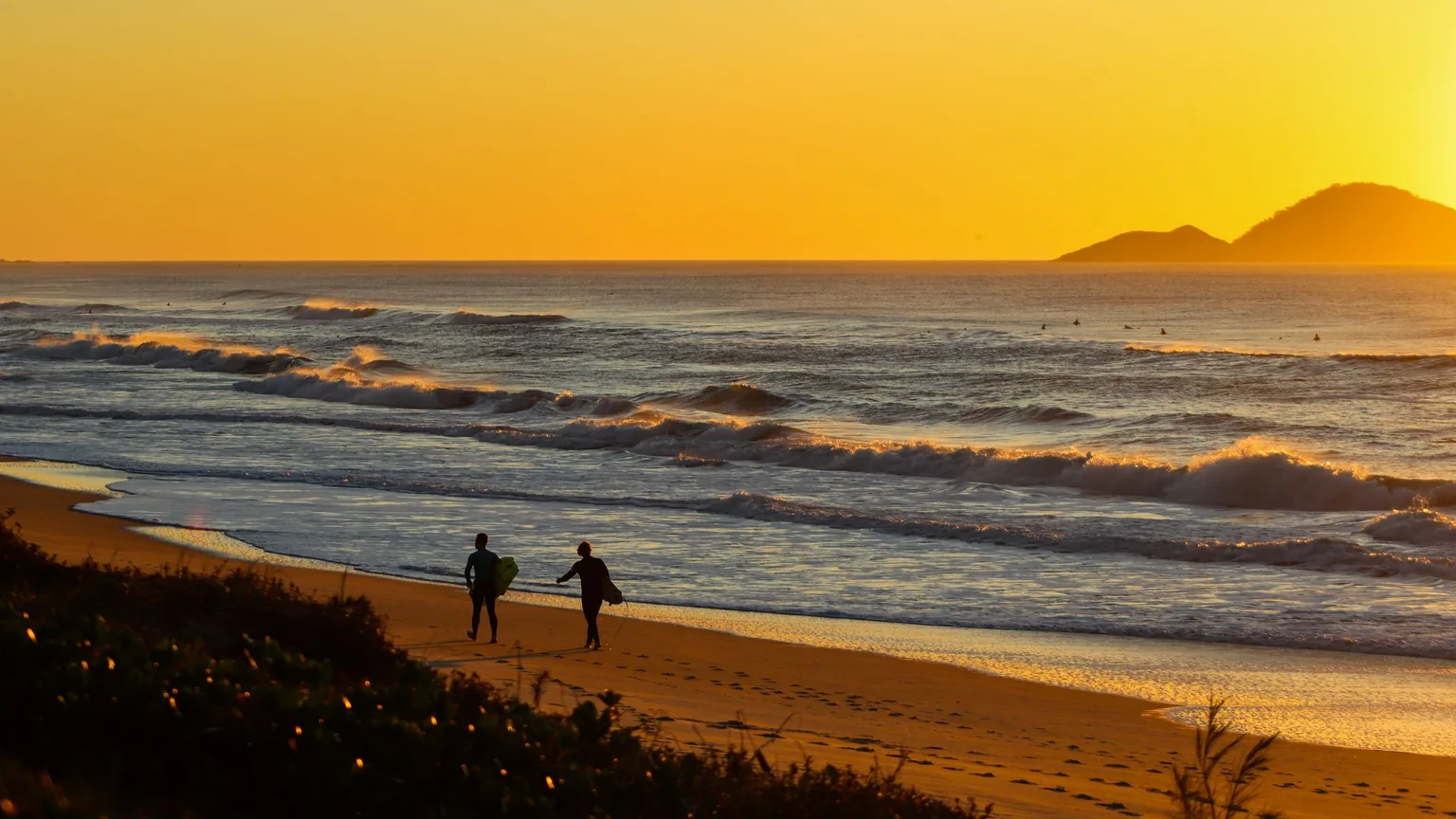 Two surfers walking along the beach at sunrise