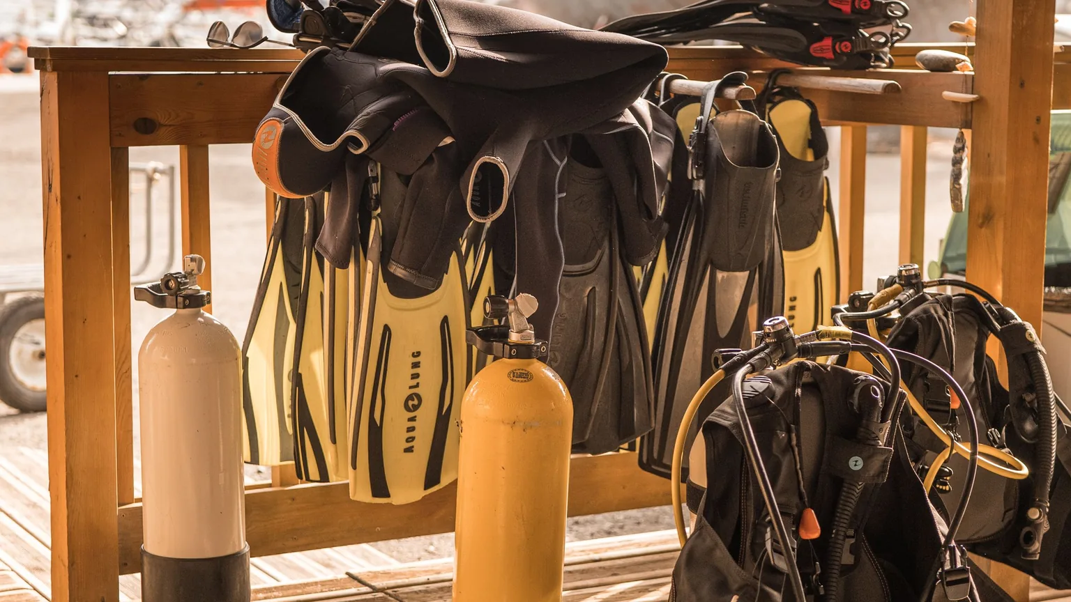 Scuba tanks, fins and wetsuits laid out on the deck of a dive shop before a trip